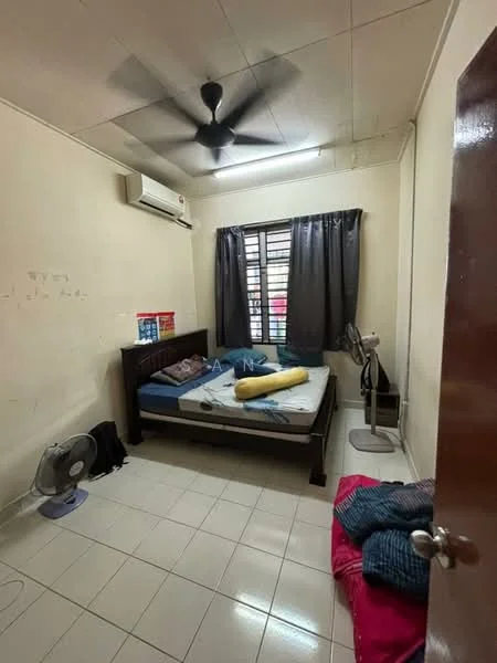 Bedroom features: single bed with mattress, blue bedsheet, yellow bolster, white tiled flooring, ceiling fan, wall-mounted split AC, black curtains, window with grille, wall-mounted fan, pink bedding on floor, wooden bed frame, plain cream walls.