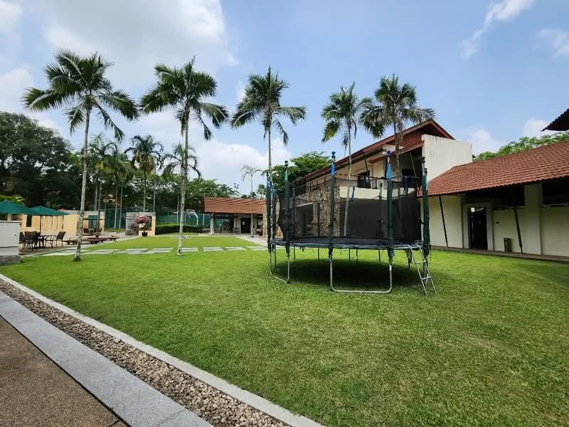 Exterior type: landscape garden; features: manicured lawn, trampoline, palm trees, paved walkway, two-storey building, red tile roof, outdoor seating area, surrounded by greenery; style: tropical-modern.