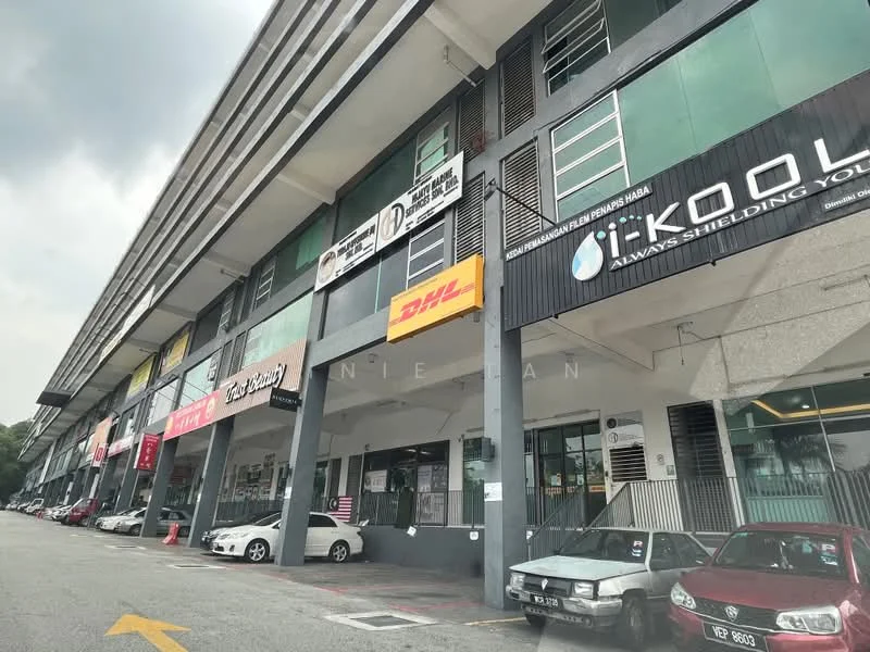Exterior type: shophouse; features: grey painted facade, glass windows, signage for various businesses, covered walkway, parking area in front, multiple storeys, balconies on upper levels, concrete columns, visible vehicles parked, urban setting; style: modern.