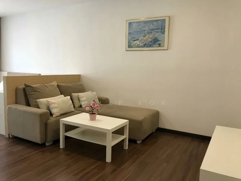 Living features: L-shape sectional sofa in beige, decorative cushions, white coffee table, framed artwork on wall, wooden flooring, neutral painted walls, natural light from window, small potted plant on table; style: modern.