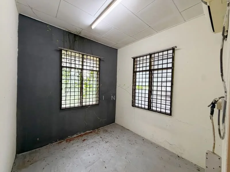 Room features: grey accent wall, white painted walls, two windows with metal grilles, concrete flooring, ceiling with fluorescent lighting, visible plant growth on walls, no visible furniture or decor.