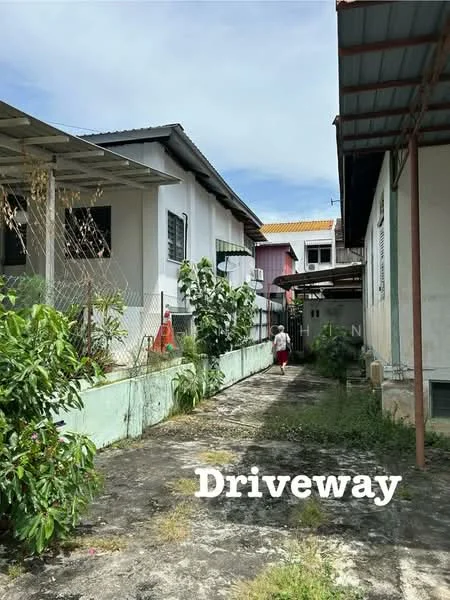 Exterior type: linked terrace house; features: concrete driveway, fenced garden area, mature shrubs, single-storey buildings, metal roof, side walkway, exposed brick wall, surrounding greenery; style: traditional.