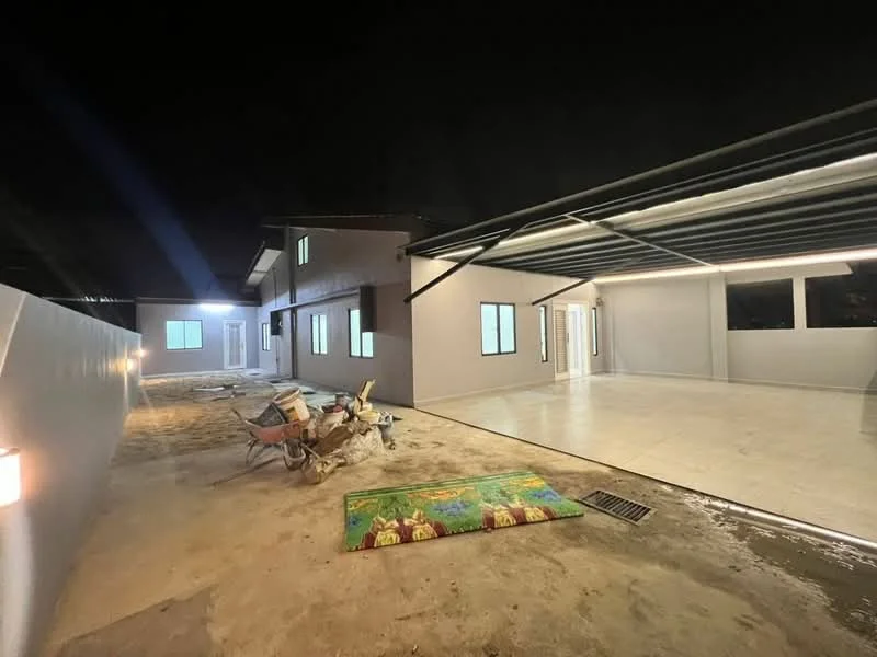 Exterior type: detached bungalow; features: flat roof, white painted facade, large windows, outdoor patio area, paved flooring, landscaped garden area, exposed concrete wall, construction materials visible, night lighting, open space, driveway area; style: modern.