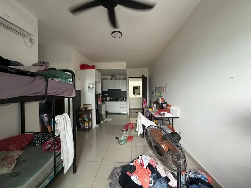 Room features: bunk bed with green bedding, single bed with patterned bedding, ceiling fan, wall-mounted air conditioning unit, white painted walls, glossy tile flooring, kitchenette with cabinets, refrigerator, kitchen countertop, messy floor with clothes, open doorway leading to another room, various kitchen appliances on countertop.