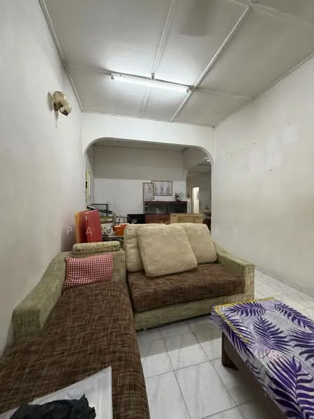 Living features: white painted walls, tile flooring, sofa with beige upholstery, sectional sofa with brown fabric, coffee table with floral pattern, wall-mounted light fixture, arched doorway, visible kitchen area in background.