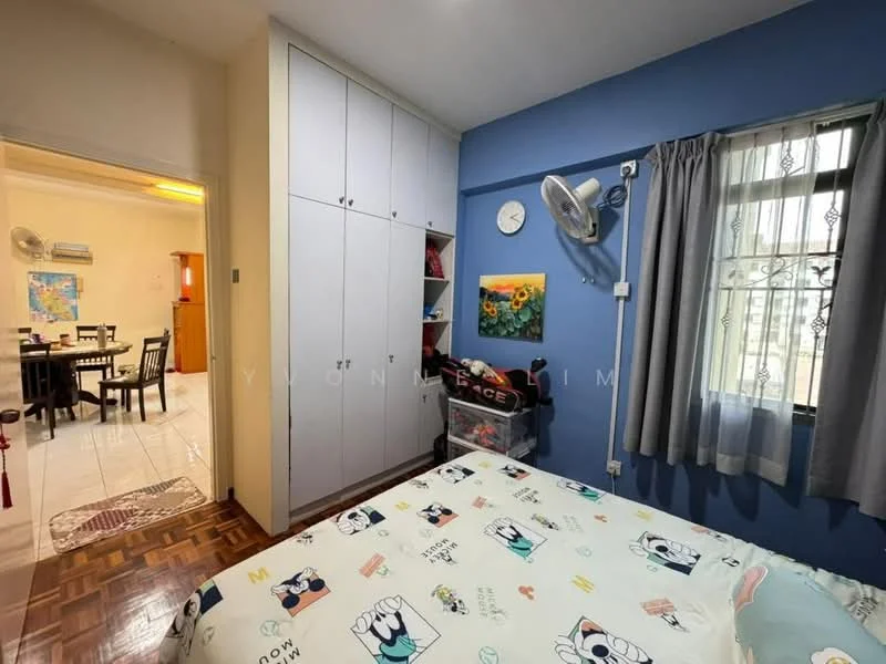 Bedroom features: blue painted walls, wooden flooring, built-in wardrobe with sliding doors, wall-mounted fan, window with sheer curtains, bed with patterned bedding, decorative wall clock, framed artwork, ceiling light fixture; style: modern. Room features: open doorway leading to dining area, visible dining table and chairs, air conditioning unit.