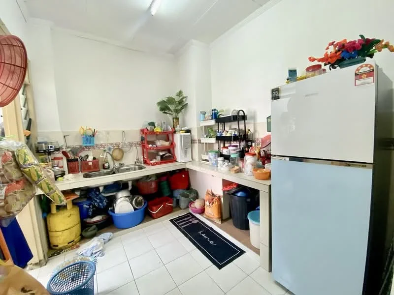 Kitchen features: single-bowl stainless-steel sink, chrome pull-down faucet, white tiled backsplash, white laminate countertop, built-in cabinetry, freestanding refrigerator in light blue, various kitchen utensils and pots, open shelving, floor tiles in white, red plastic storage containers, green potted plant, kitchen mat with decorative pattern.