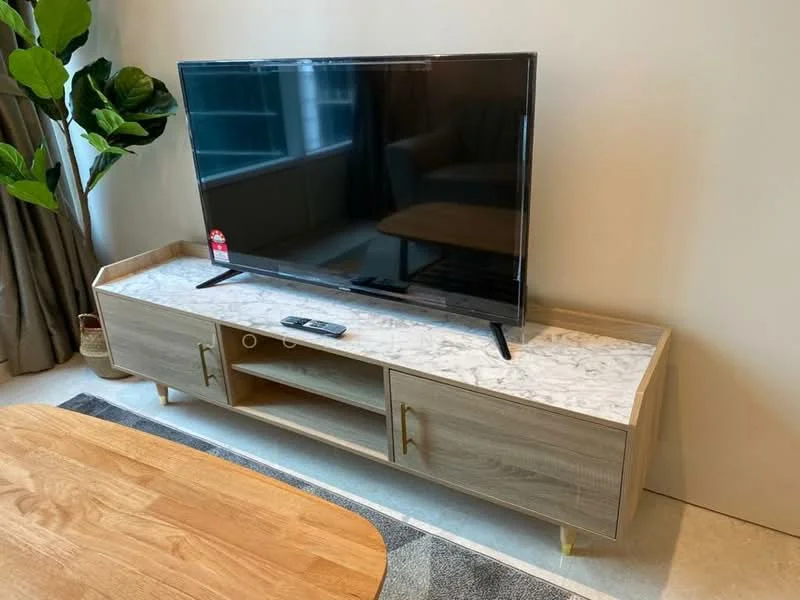 Living features: wooden TV console with marble top, black flat-screen TV, remote control on console, green potted plant, beige sofa in background, light-colored area rug, curtains, light-colored wall; style: modern.
