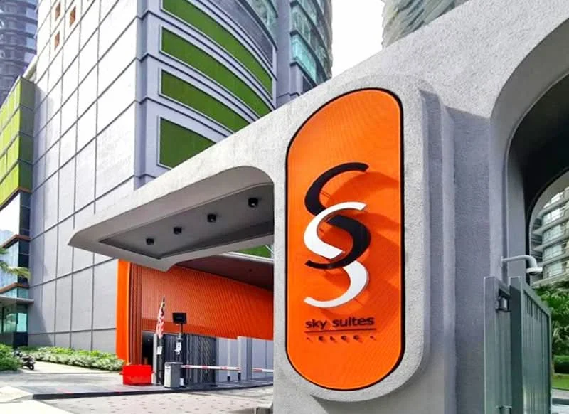 Exterior type: high-rise condominium; features: orange painted facade, glass curtain wall, green accent panels, modern entrance structure, landscaped garden area, security gate, driveway with interlocking pavers; style: modern.