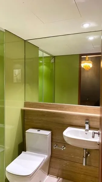 Bathroom features: green glass walls, wood paneling, white toilet, single-sink vanity, chrome faucet, large mirror, recessed lighting, chandelier; style: modern.