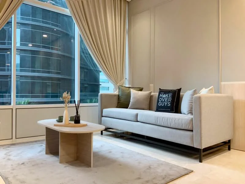 Living features: 3-seater fabric sofa in light grey, decorative throw pillows, coffee table with round top, area rug in neutral tones, floor-to-ceiling windows, sheer curtains, wall-mounted decor, light-colored walls, wooden paneling, natural light from windows; style: modern; view: city.