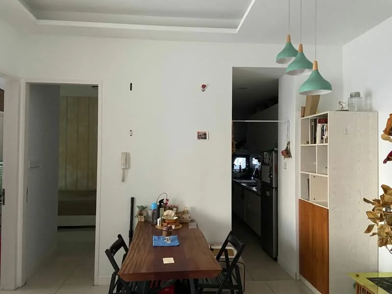 Dining features: white painted walls, tile flooring, dining table with chairs, green pendant lights, built-in shelving unit, decorative items on shelves, wall-mounted intercom, open doorway to kitchen; style: modern. Kitchen features: white cabinetry, stainless-steel appliances, countertop, open layout to dining area; style: modern.