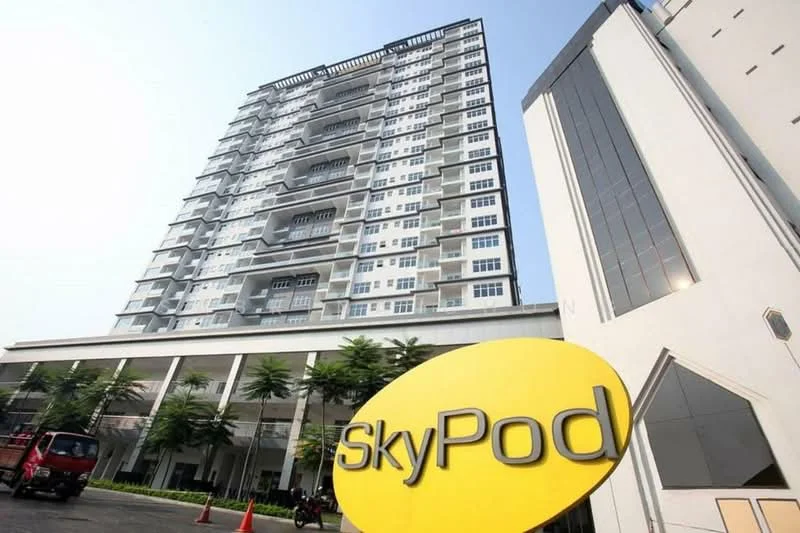 Exterior type: high-rise condominium; features: glass curtain wall, white painted facade, recessed balconies, approximately 10-storey high-rise, manicured landscaping, signage with name 'SkyPod', parking area, surrounded by mature greenery; style: modern.
