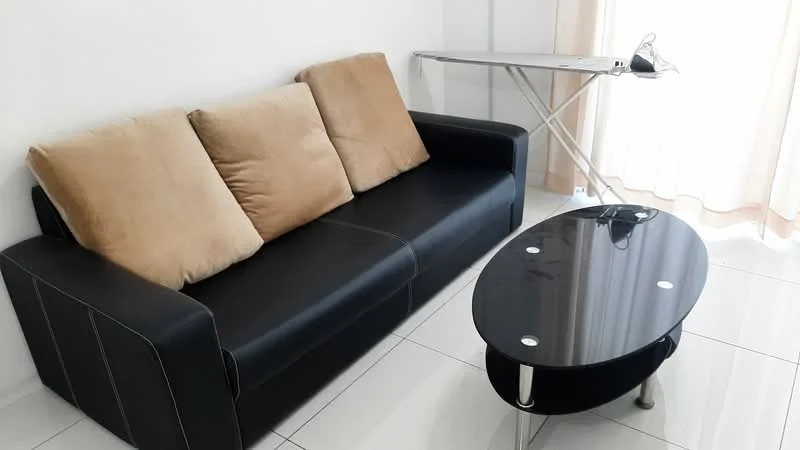 Living features: 3-seater black leather sofa with beige cushions, glass coffee table with rounded edges, white walls, white tiled flooring, floor-to-ceiling window with sheer curtains, ironing board, power outlet on table; style: modern.