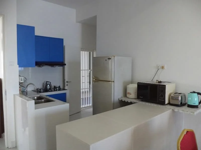 Kitchen features: blue cabinetry, stainless-steel sink, chrome faucet, 4-burner gas hob, built-in oven, stainless-steel fridge, microwave, toaster, kettle, white countertop, white walls, tile backsplash, open layout; style: modern.