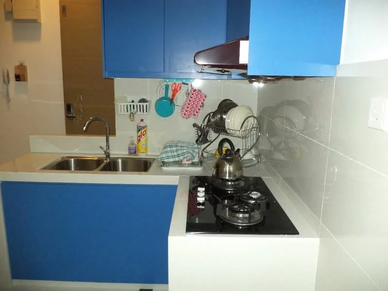 Kitchen features: blue cabinetry, white countertop, double-bowl stainless-steel sink, chrome pull-down faucet, built-in gas stove with 2 burners, exhaust hood, dish rack, kettle, various kitchen utensils, wall-mounted storage rack, white tiled backsplash, open shelving; style: modern.