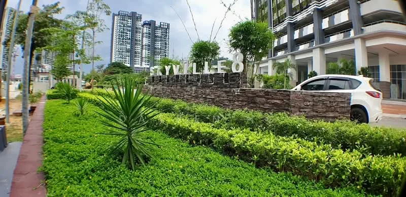 Exterior type: high-rise condominium; features: landscaped garden with manicured lawn, stone-clad feature wall, modern signage with the name 'STYLLEO', paved walkway, surrounded by greenery, parking lot with visible vehicle, multi-storey buildings in the background, tropical landscaping with palm trees; style: modern.