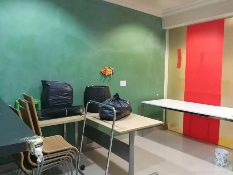 Room features: green painted walls, light-colored flooring, wooden tables, stacked chairs, black bags, decorative wall art, table against wall.