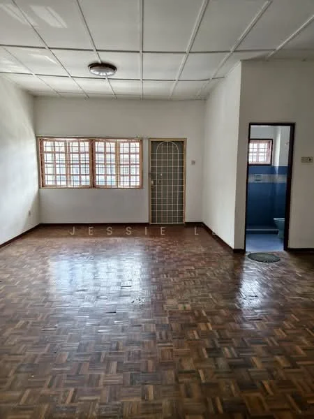 Room features: parquet wood flooring, white painted walls, ceiling light fixture, grid ceiling, two windows with wooden frames, doorway leading to another room, door with metal grille, visible bathroom door, round floor mat.
