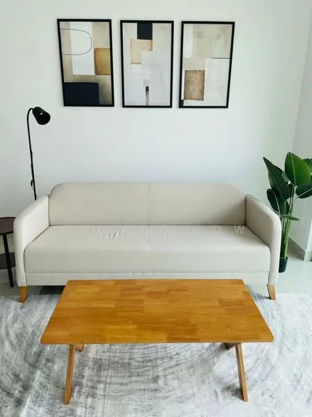 Living features: beige fabric sofa, wooden legs on sofa, wooden coffee table, area rug with geometric pattern, floor lamp with black shade, framed abstract artwork on walls, potted plant, white painted walls, light-colored flooring, natural light from windows; style: modern.
