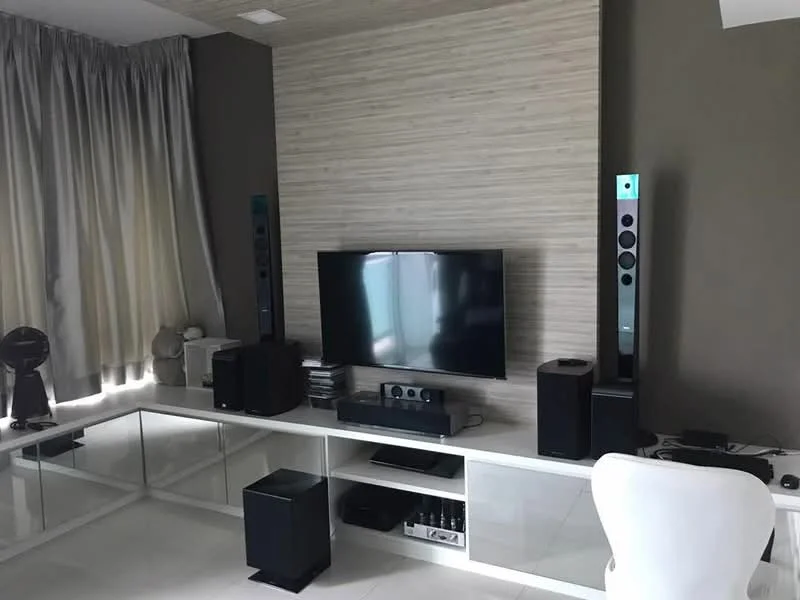 Living features: flat-screen TV, white media console, black sound system speakers, tall speaker towers, light grey accent wall, textured wall paneling, floor-to-ceiling curtains, white ceramic decorative items, white chair, polished tile flooring; style: modern.