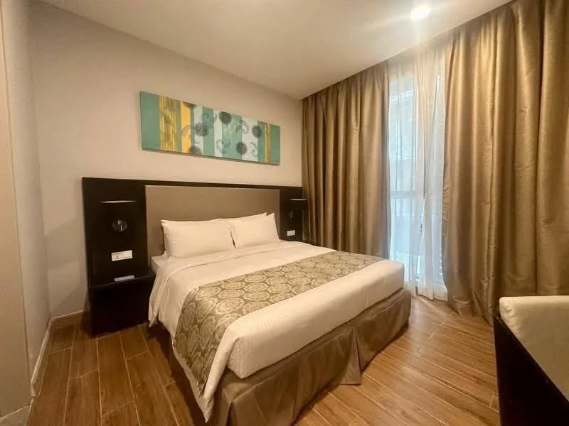 Bedroom features: queen-size bed with upholstered headboard, white bedding with decorative throw, wooden bedside tables, table lamps on each side, floor-to-ceiling windows with sheer curtains, wooden flooring, decorative wall art, beige accent wall, built-in wardrobe, recessed ceiling lights; style: modern.