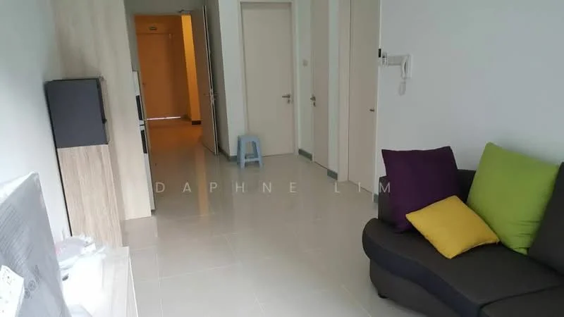Room features: grey fabric sofa, green and yellow accent pillows, light-colored walls, white tiled flooring, wooden cabinet, doorway leading to hallway, doorway leading to another room, small blue stool, wall-mounted TV, light switch on wall; style: modern.