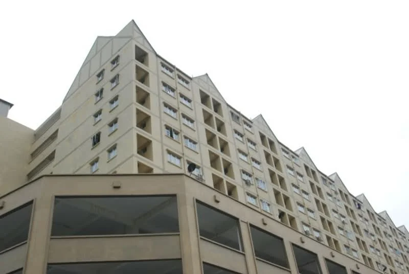 Exterior type: low-rise apartment block; features: cream painted facade, recessed balconies, multiple windows, sloping roof, open-air parking area, concrete structure; style: modern.