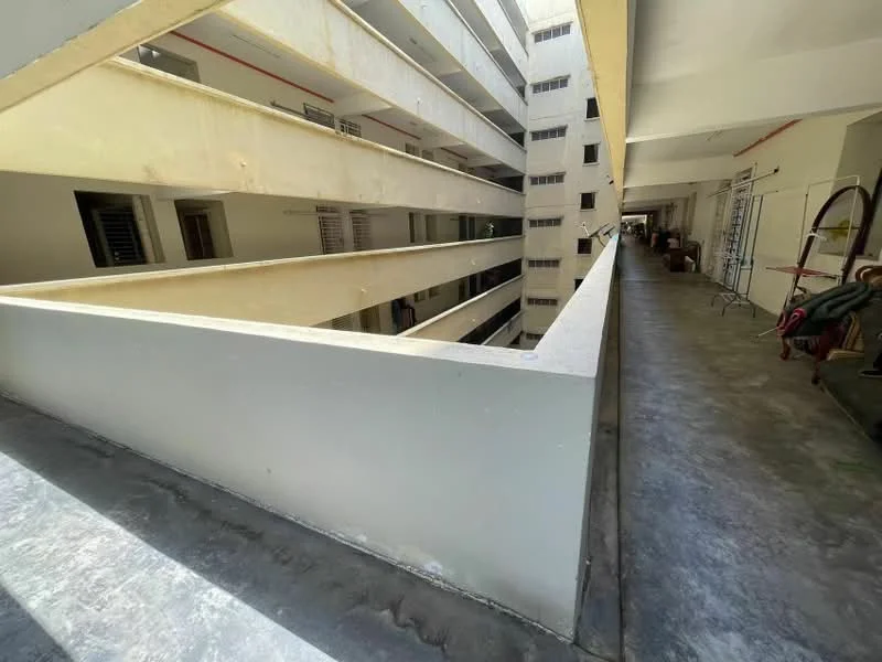 Exterior type: low-rise apartment block; features: concrete facade, open-air corridor, balconies with railings, grey painted walls, exposed concrete flooring, multiple levels, natural light from openings, utility area with storage, surrounding walls, interior courtyard view; style: modern.