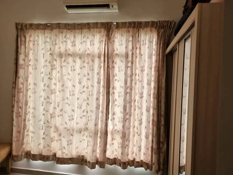 Room features: curtains with floral pattern, wall-mounted air conditioning unit, built-in wardrobe, light-colored walls, wooden flooring, window with natural light.