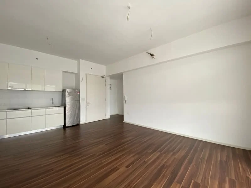 Living features: laminate flooring, white painted walls, kitchenette with white cabinetry, stainless-steel fridge, open layout, no visible ceiling fixtures, large empty wall space, neutral color scheme; style: modern.