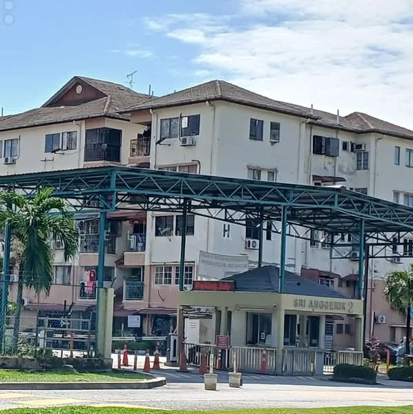 Exterior type: low-rise apartment block; features: two-storey building, green metal awning, main entrance gate, guard house at entrance, palm trees, parking area with cones, air conditioning units visible, balconies with railings, cream painted facade, surrounded by greenery; style: modern.