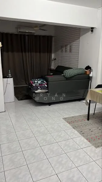 Living features: grey fabric sofa, green throw pillow, stack of folded clothes on sofa, white tiled flooring, ceiling fan, curtains in brown, wall-mounted light, white painted walls, decorative wall with horizontal slats, dining table with beige tablecloth, area rug with geometric pattern.
