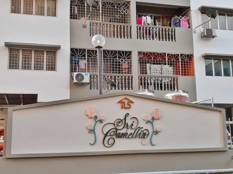 Exterior type: low-rise apartment block; features: white painted facade, balconies with metal railings, air conditioning units visible, signage with floral design, outdoor lighting fixture, clothes hanging on balcony, windows with grilles; style: modern.