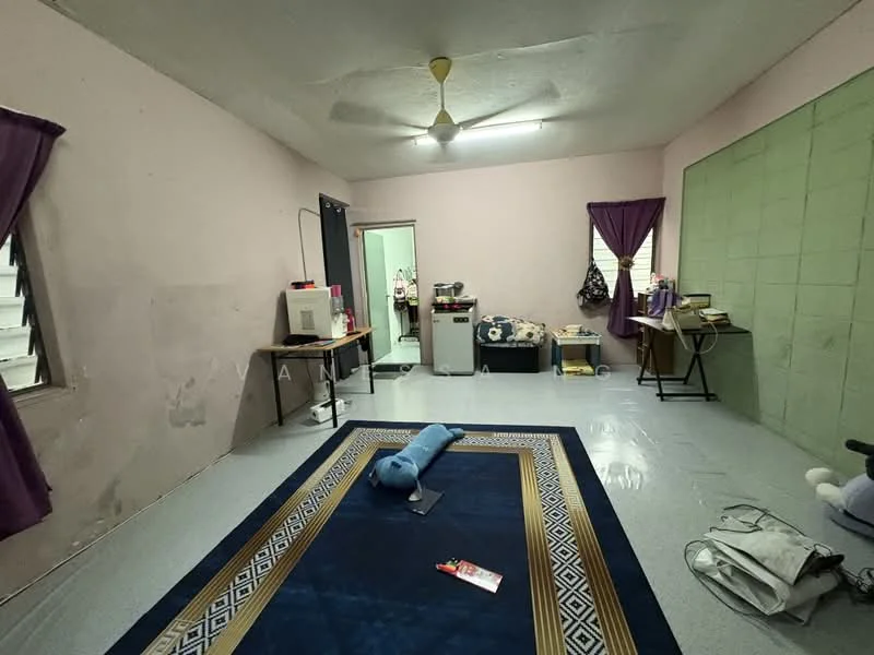 Room features: light blue painted walls, green accent wall, ceiling fan, vinyl flooring, window with white grilles, purple curtains, wooden table, folding chair, area rug with geometric pattern, storage boxes, doorway leading to another room.