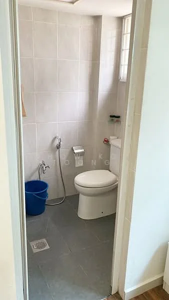 Bathroom features: white tiled walls, grey tiled flooring, one-piece toilet, handheld shower, shower hose, floor drain, small window, blue plastic bucket.