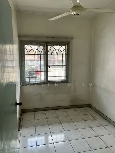 Room features: white painted walls, tiled flooring, window with grid pattern, ceiling fan, light switch, door with knob, corner of room visible, natural light from window.
