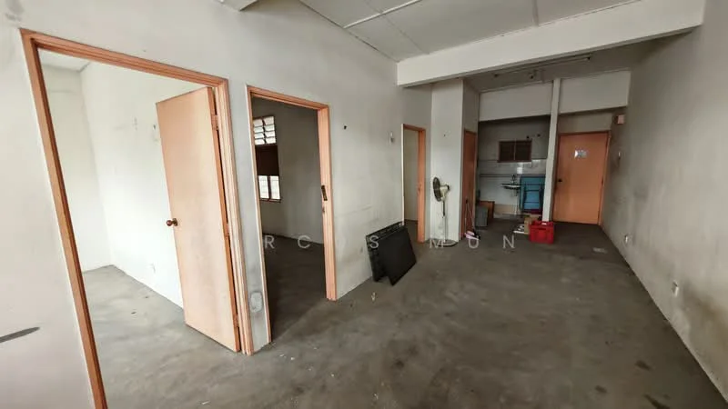 Room features: plain white walls, concrete flooring, multiple doorways, ceiling with fluorescent lighting, wall-mounted fan, empty space, no visible furniture, unfinished appearance; style: minimalist.