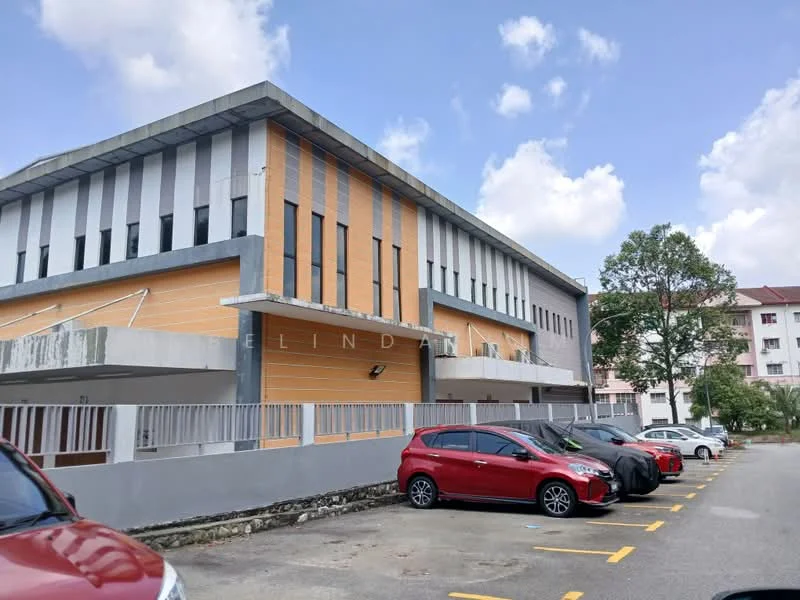 Exterior type: low-rise apartment block; features: orange painted facade, grey accent panels, multiple storeys, parking lot in front, manicured landscaping, surrounded by residential buildings, visible trees, clear blue sky; style: modern.