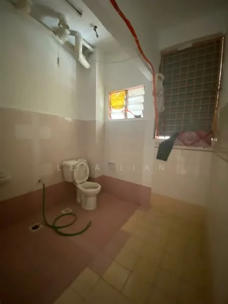 Bathroom features: white ceramic toilet, pink tiled walls, cream tiled flooring, window with security bars, exposed plumbing, green hose on floor, light fixture on ceiling.