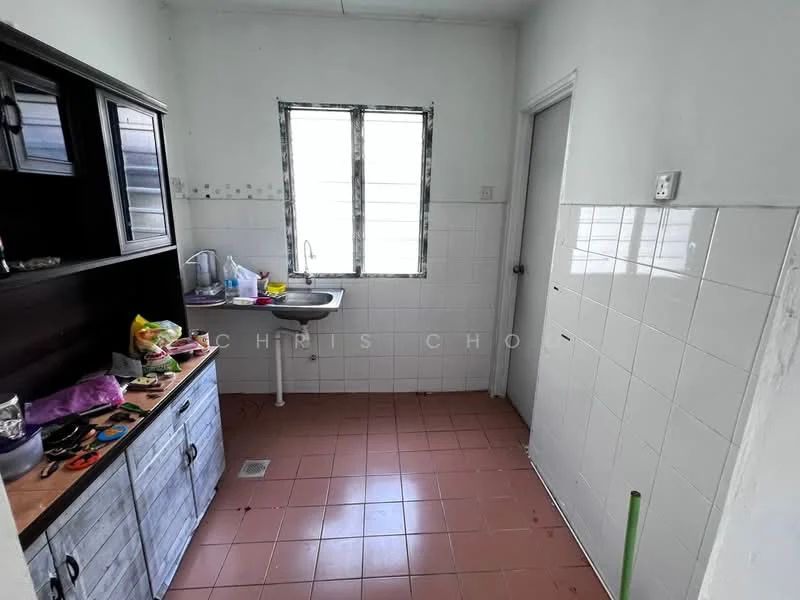 Room features: white painted walls, white tiled backsplash, brown wooden cabinetry, single-bowl stainless-steel sink, chrome faucet, red ceramic tile flooring, window with horizontal slats, countertop with clutter, door leading to another room.