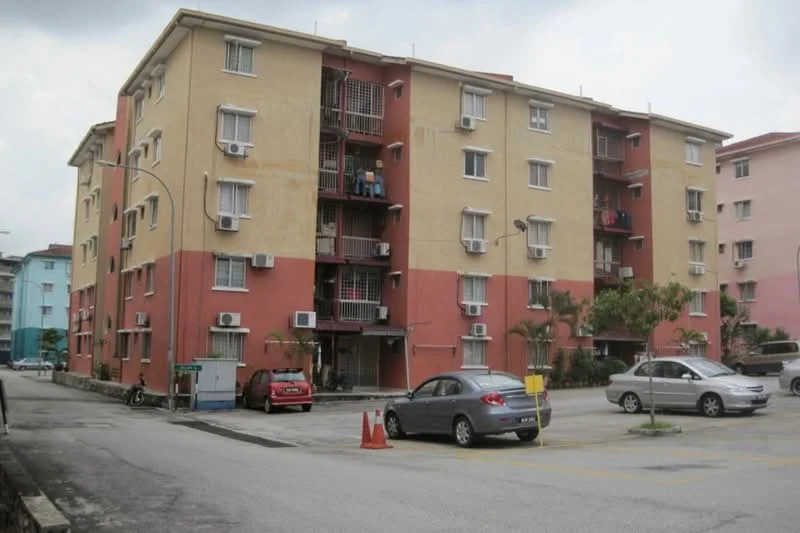 Exterior type: low-rise apartment block; features: yellow and red painted facade, multiple wall-mounted split AC units, balconies with railings, parking lot with marked spaces, landscaped area with small plants, two-storey building, surrounded by paved driveway; style: modern.