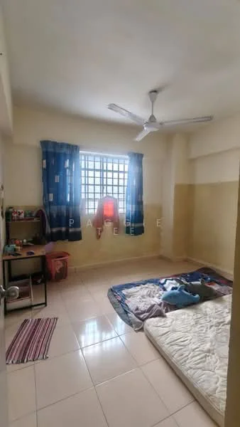Bedroom features: single bed mattress on the floor, ceiling fan, window with metal grille, blue curtains with geometric pattern, cream painted walls, tiled flooring, wooden study table, small shelving unit, area rug with striped pattern.