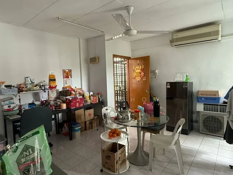 Room features: white painted walls, tiled flooring, ceiling fan, wall-mounted air conditioning unit, round dining table, plastic chairs, refrigerator, open shelving, storage boxes, decorative items on shelves, fruit bowl with oranges, door leading to outside, window with grille.