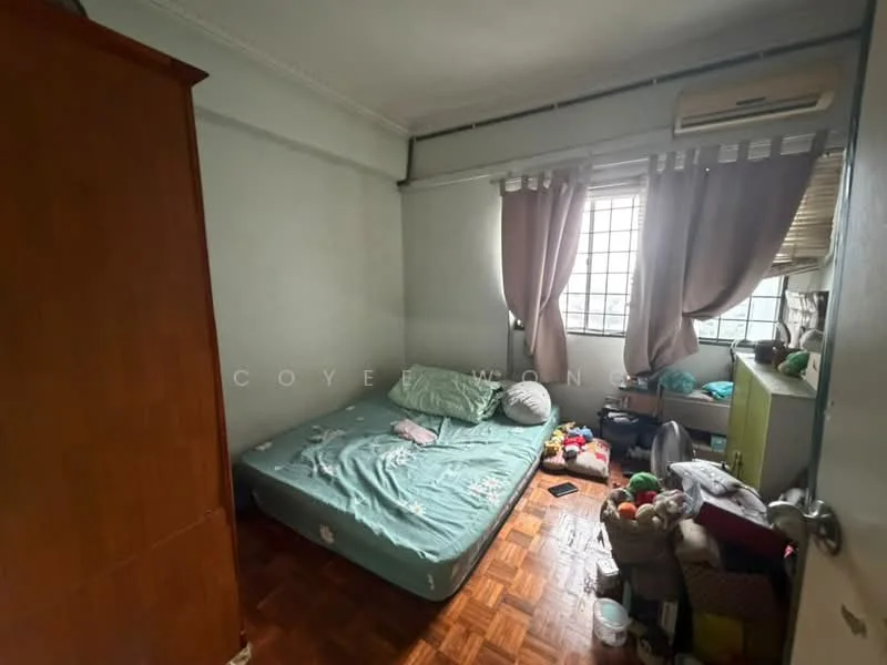 Bedroom features: wooden flooring, green mattress on bed frame, brown wooden wardrobe, window with sheer curtains, air conditioning unit, decorative pillows, stuffed toys on floor, green bedside table.