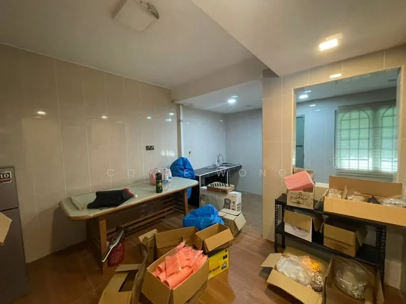 Room features: grey tiled walls, light brown wooden flooring, single-bowl stainless-steel sink, chrome pull-down faucet, countertop with storage underneath, window with natural light, multiple cardboard boxes, plastic bags, kitchen appliances visible, open layout.