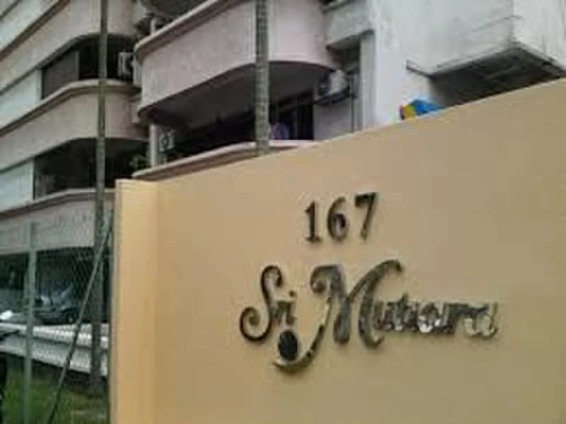 Exterior type: low-rise apartment block; features: cream painted facade, balconies with railings, visible air conditioning units, landscaped entrance, signage with name 'Sri Mutera', fenced perimeter, parking area visible, multi-storey structure; style: modern.