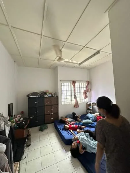 Room features: white painted walls, tiled flooring, ceiling fan, window with grid pattern, curtains, mattresses on the floor, black wooden cabinet, TV unit, clothes on a rack.