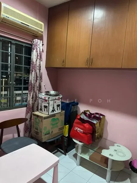 Room features: pink painted walls, white tiled flooring, window with metal grille, curtains with floral pattern, wooden cabinets, air conditioning unit, cardboard boxes, colorful bags, small table, wooden chair.