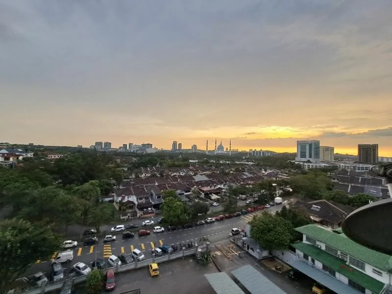 Exterior features: city skyline, sunset view, residential area with low-rise houses, greenery in foreground, road with parked cars, yellow pedestrian crossing lines; style: modern.